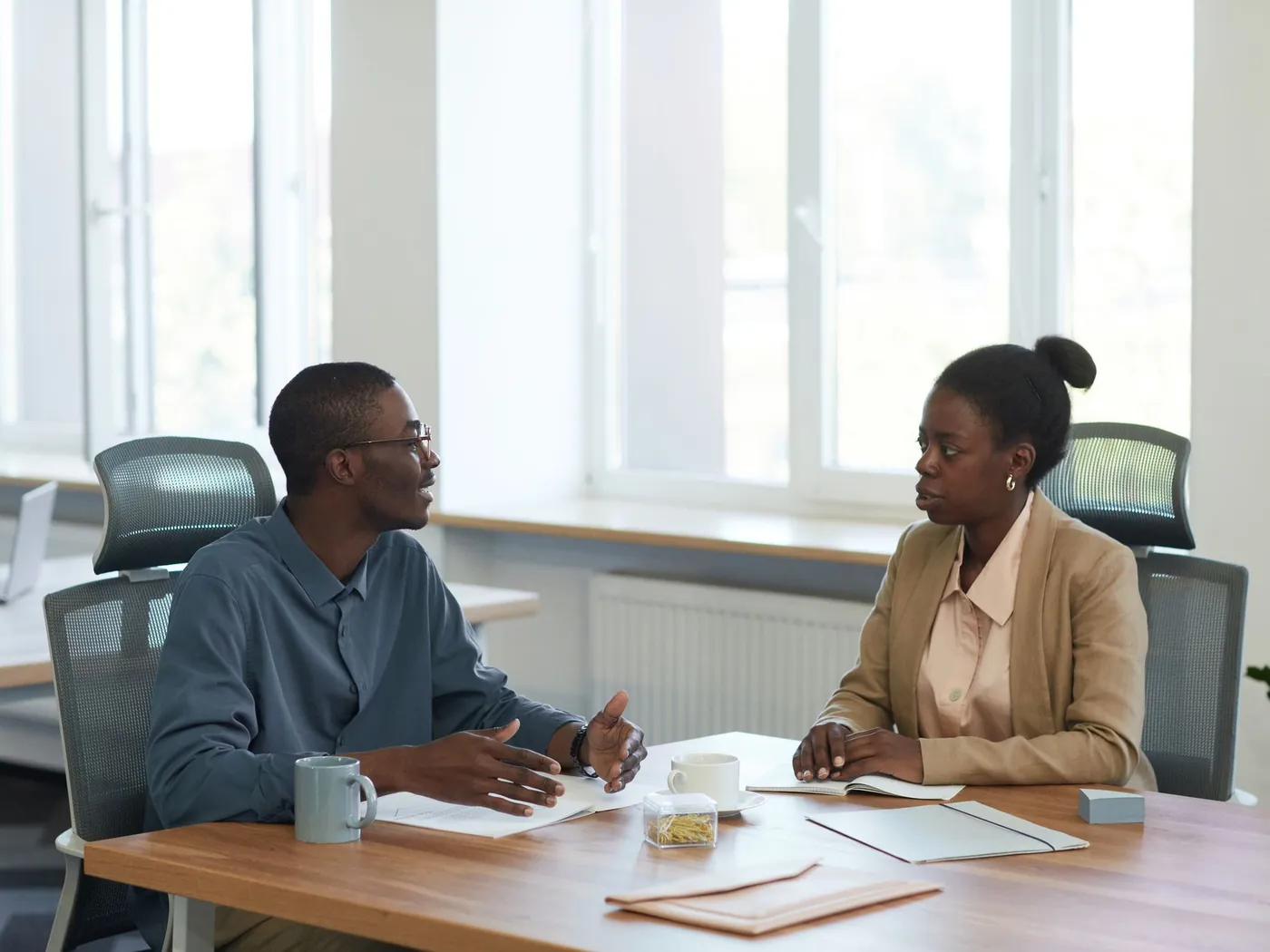 Two colleagues discussing paperwork at a desk in a bright office
