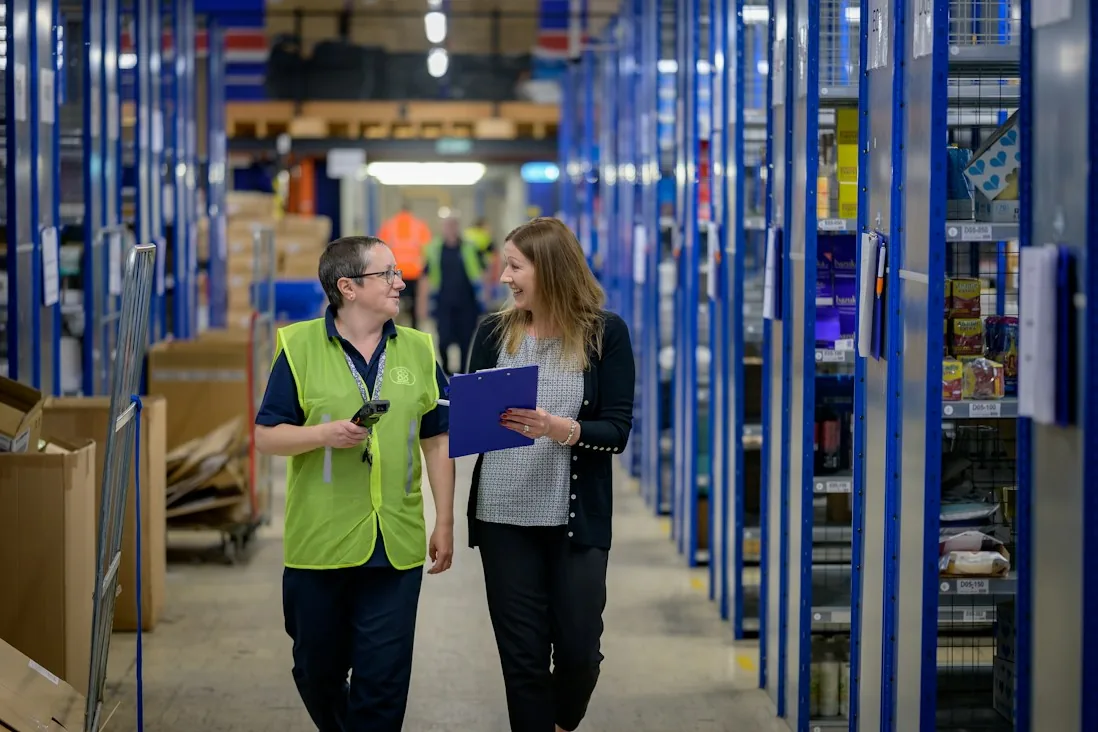 Staff walking a warehouse aisle between stocked shelves